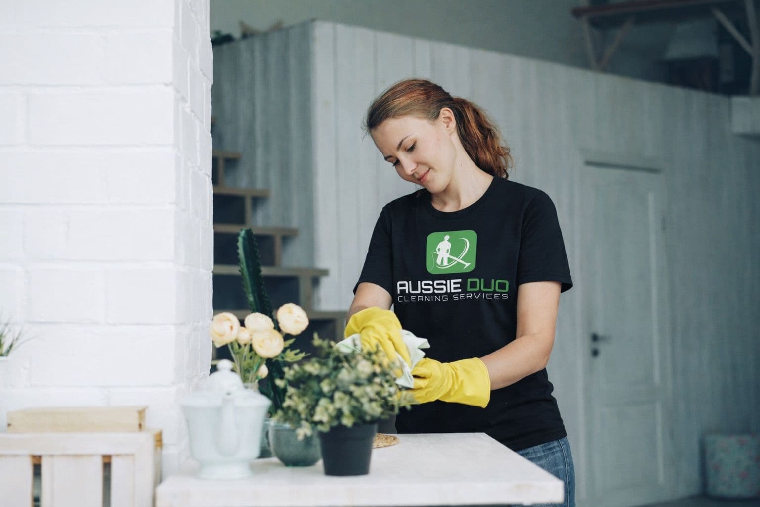Professional cleaner from Aussie Duo providing house cleaning services while dusting and tidying a home interior.
