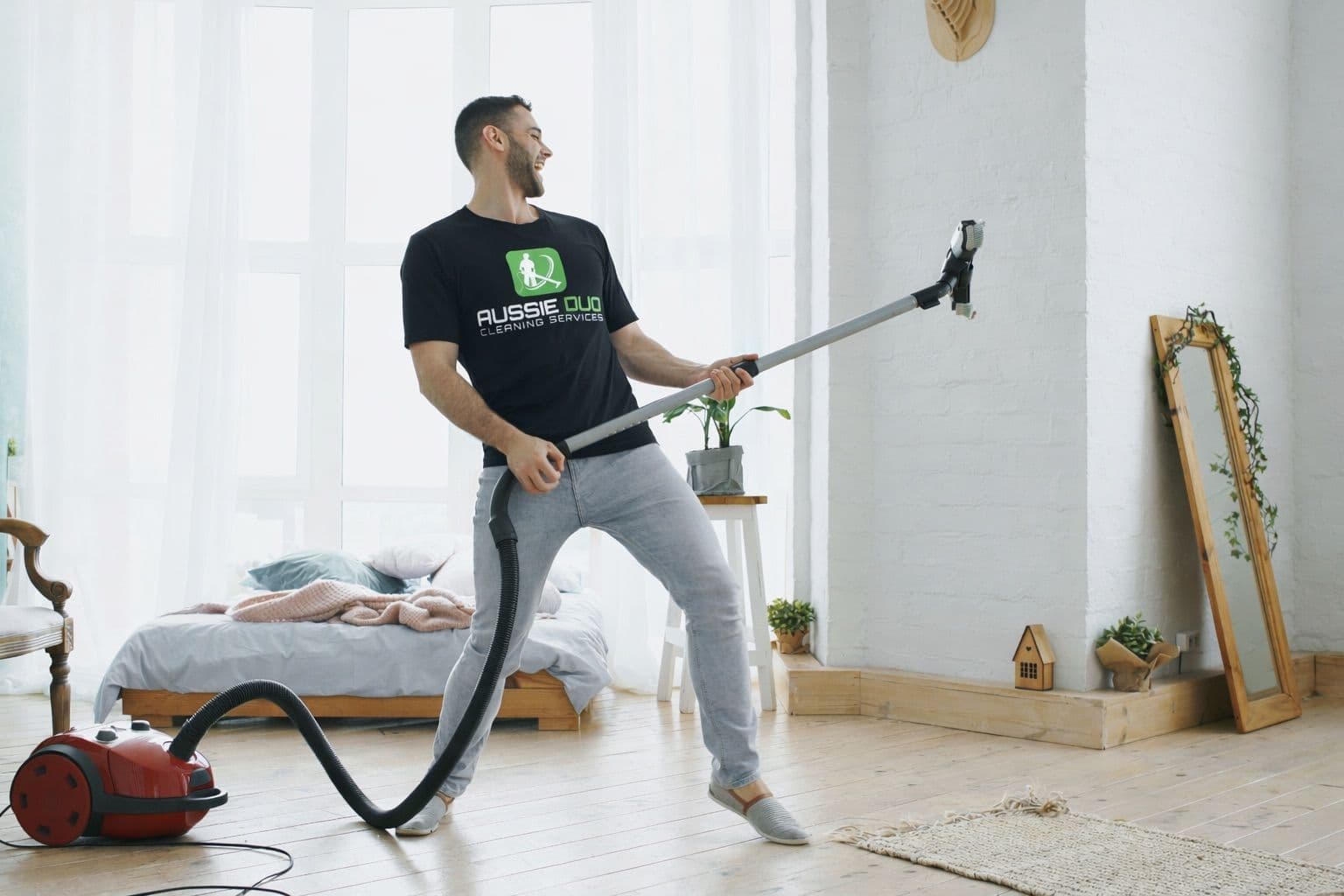 A regular house cleaner using professional vacuum equipment to clean a bedroom as part of routine home cleaning.