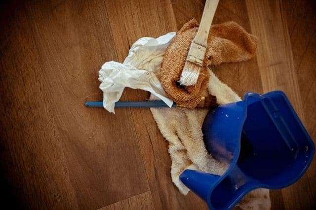 Domestic cleaning tools including cloths, brush, and dustpan placed on a wooden floor.
