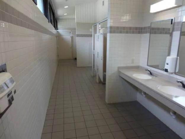 Clean public restroom with tiled walls and floors, sinks with mirrors on the right, and toilet stalls on the left.