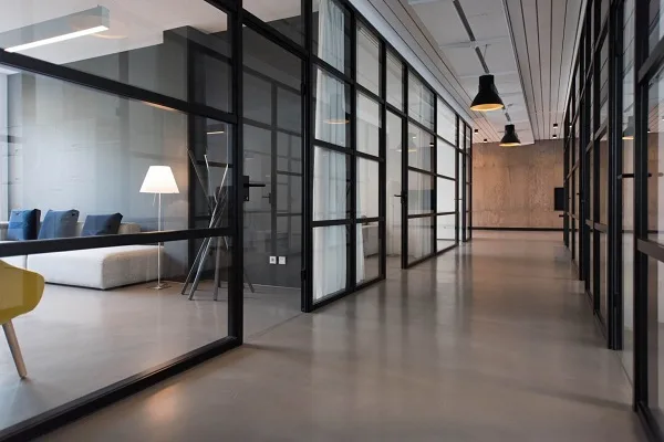 Modern office corridor with glass-walled meeting rooms and minimalistic decor.
