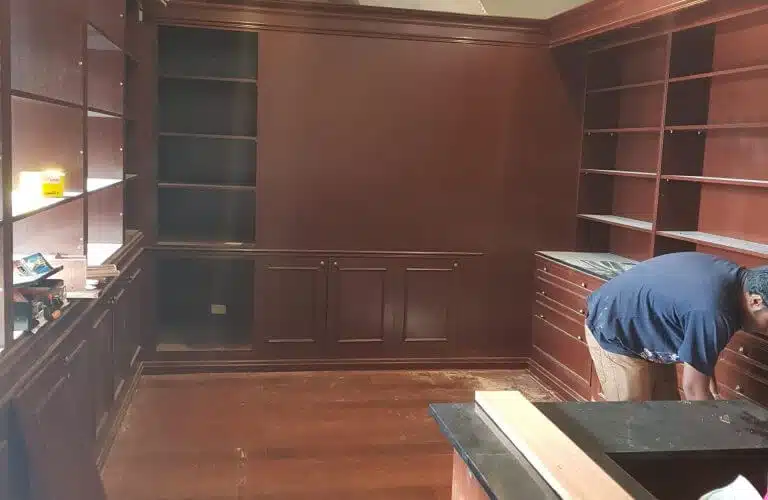 Worker cleaning up a room with dark wooden shelves and cabinetry after construction, preparing the space for use