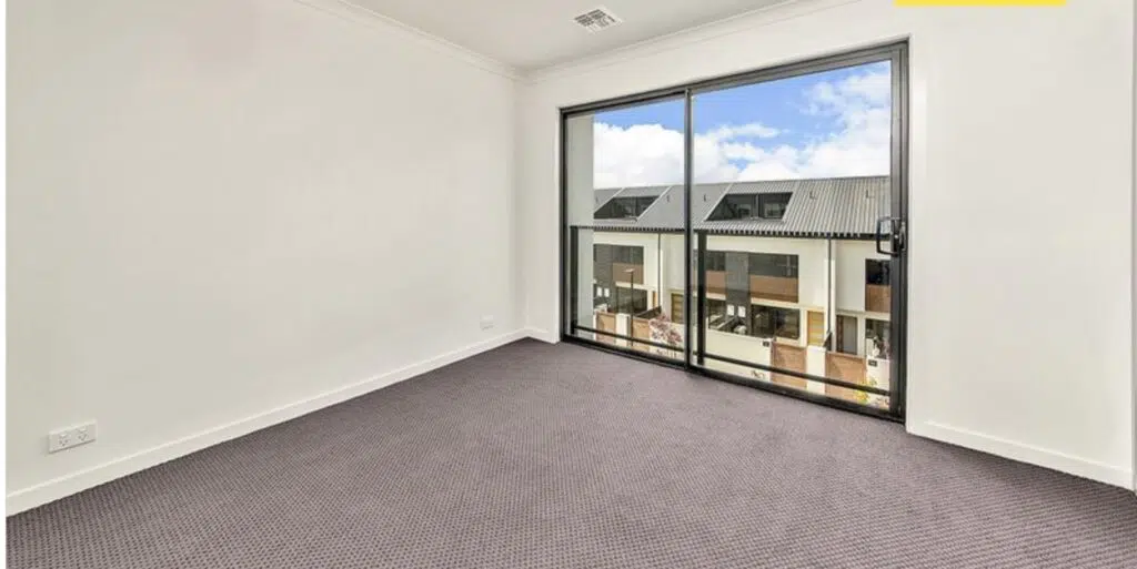 Empty modern room with carpet flooring and large window facing residential buildings.
