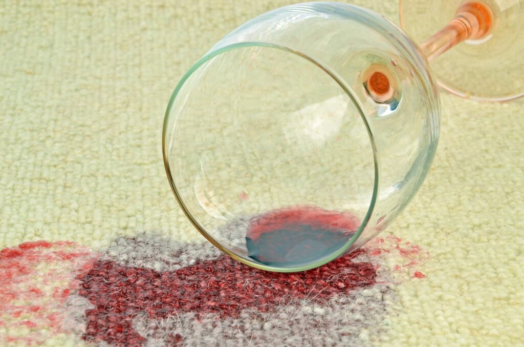 A spilled glass of red wine on a light coloured carpet.