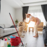 A happy cleaner high-fiving a client's dog in a spotless living room after house cleaning, with cleaning supplies visible in the foreground.