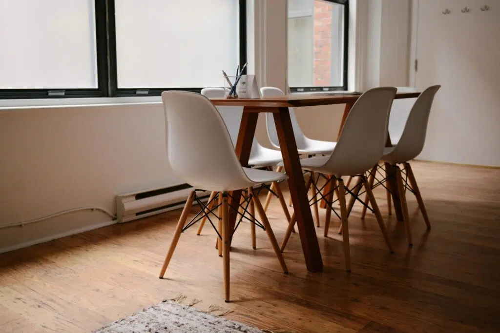 Modern wooden dining table with six white chairs in a minimalist room.